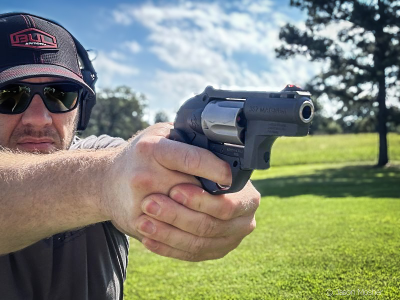 A man wearing a black hat and black sunglasses, shooting the Taurus 605 Protector Poly at the range. 