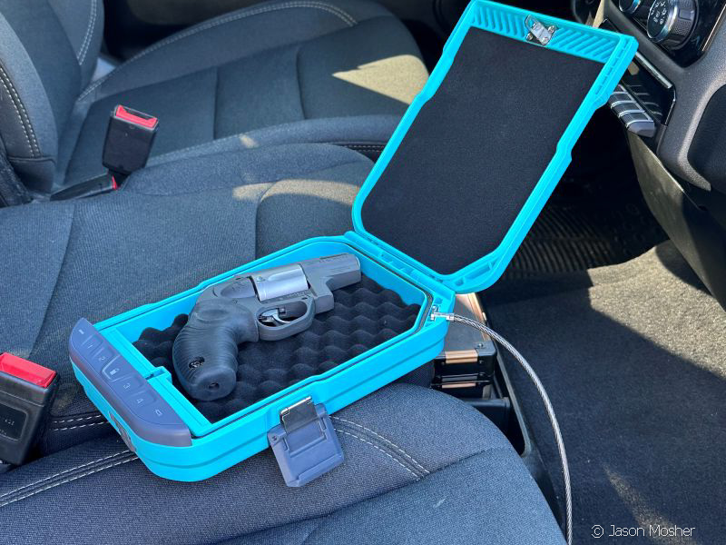 A teal colored small, portable safe on the seat of a truck, open with a revolver in the safe. 