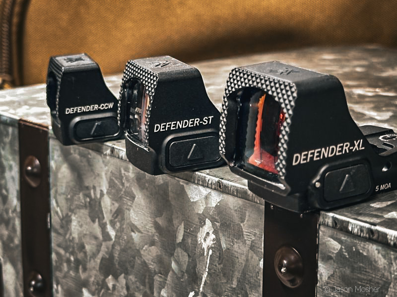 Three Vortex red dot optics lined up on a metal surface showing the different sizes: Defender-CCW, Defender-ST, and Defender-XL