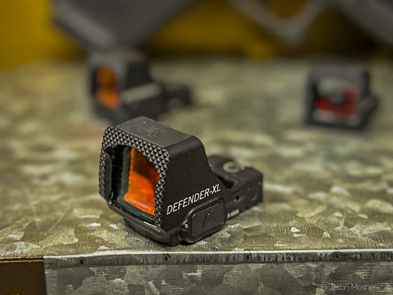 The Vortex Defender XL red dot optic sitting on a metal surface, not attached to a gun. 