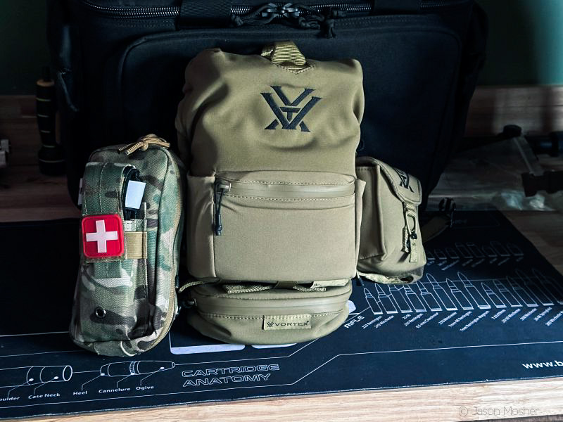 A green chest pack with several pockets sitting on a table in a dark room. 