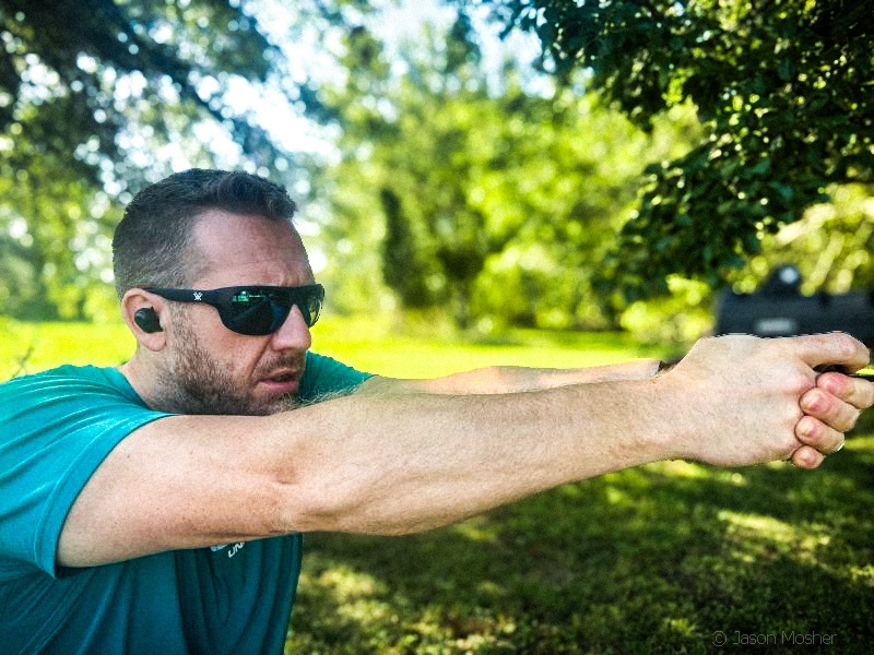 A person wearing a teal-colored shirt with short blond hair shooting a handgun while wearing a pair of Vortex JACKL sunglasses. 