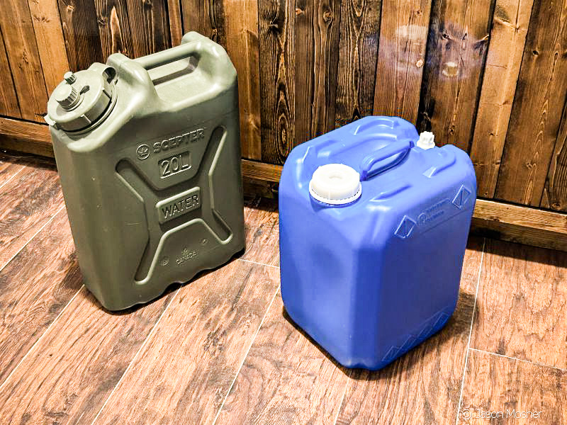 A green water storage container next to a blue wtaer container in front of some wood cabinets.
