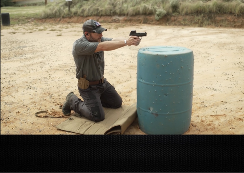 Rick Hogg of War HOGG Tactical is demonstrating a 2 knee pistol kneeling position behind a pickle barrel to simulate cover
