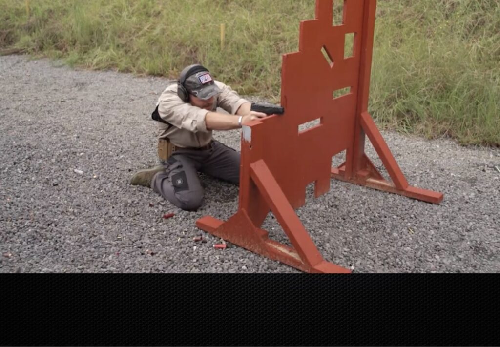 Rick Hogg of War HOGG Tactical is demonstrating two-knee pistol shooting position behind a V-TAC barricade and using the barricade for support