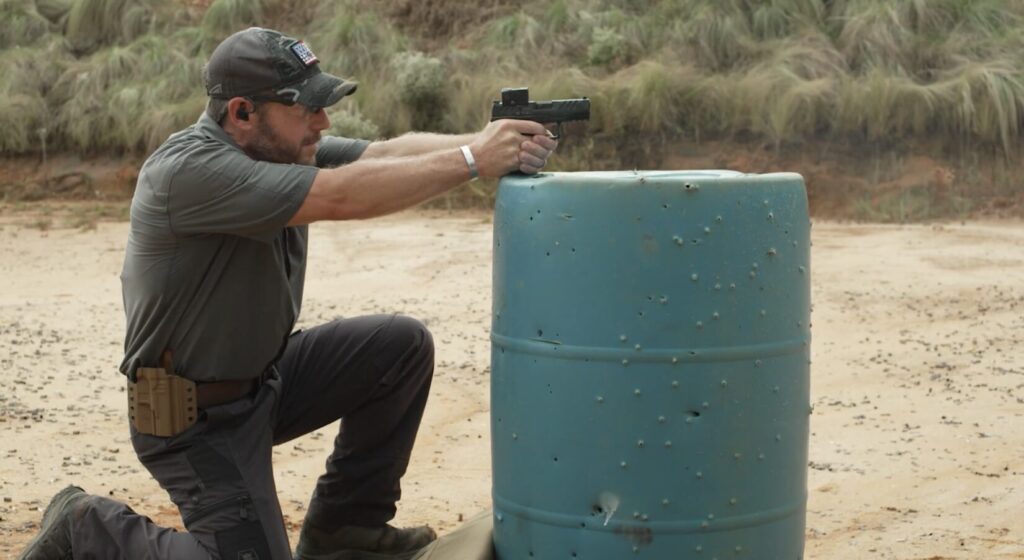 Rick Hogg of War HOGG Tactical demonstrating a supported kneeling pistol shooting position using a pickle barrel for support