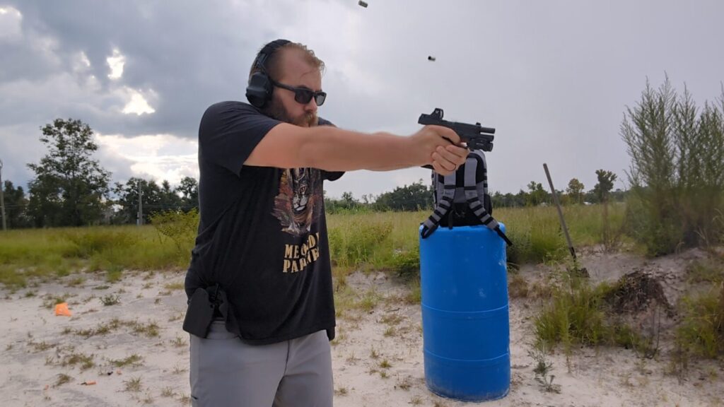 A man at an outdoor shooting range aims a Ruger RXM pistol, with two spent casings visible in mid-air.