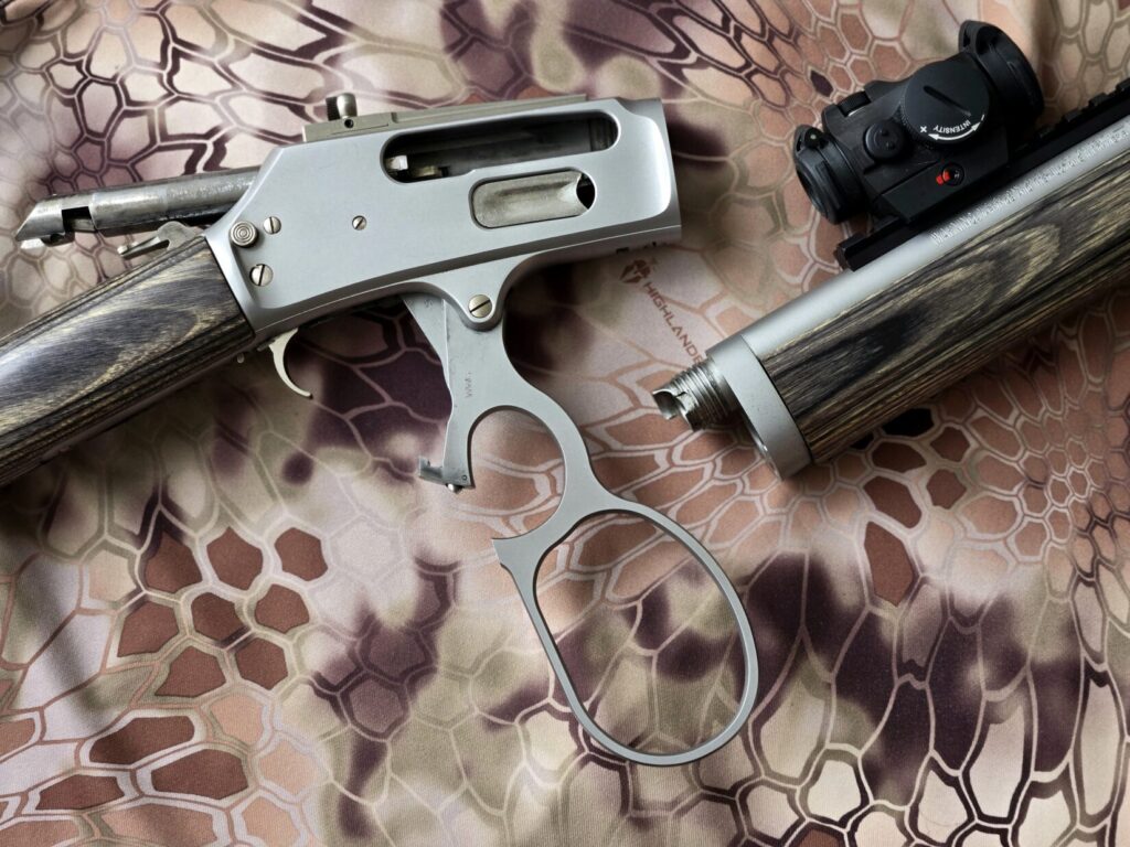 A take down lever action rifle with aimpoint red dot on a kryptek camouflage backdrop