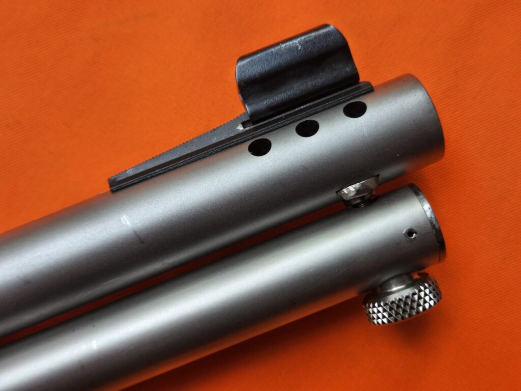 Close up shot of a ported rifle barrel and hooded front sight on a blaze orange backdrop.