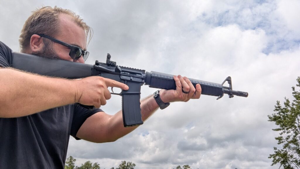 Man wearing sunglasses, holding a black dissipator rifle and aiming it towards the sky.
