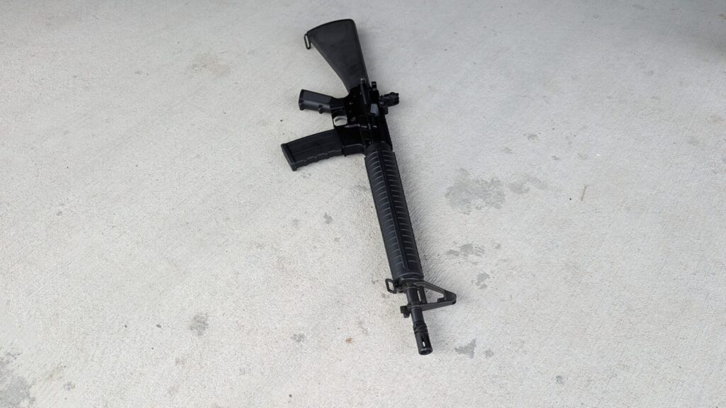 A black dissipator rifle with a fixed stock and a magazine, lying on a concrete surface