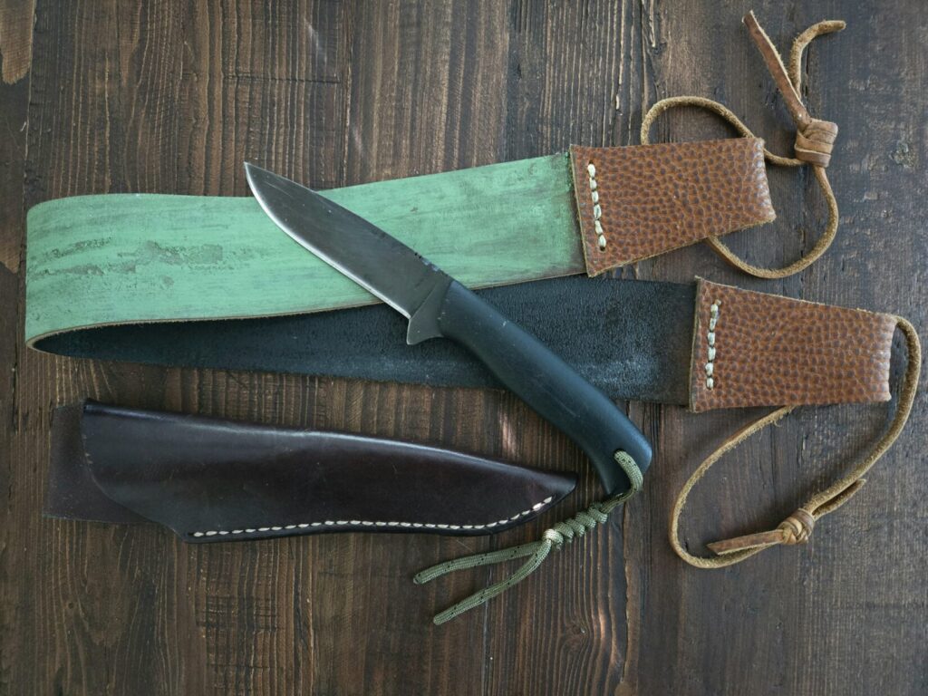 A Winkler knives mentor blade on a wooden table with a leather strop and a sheath nearby