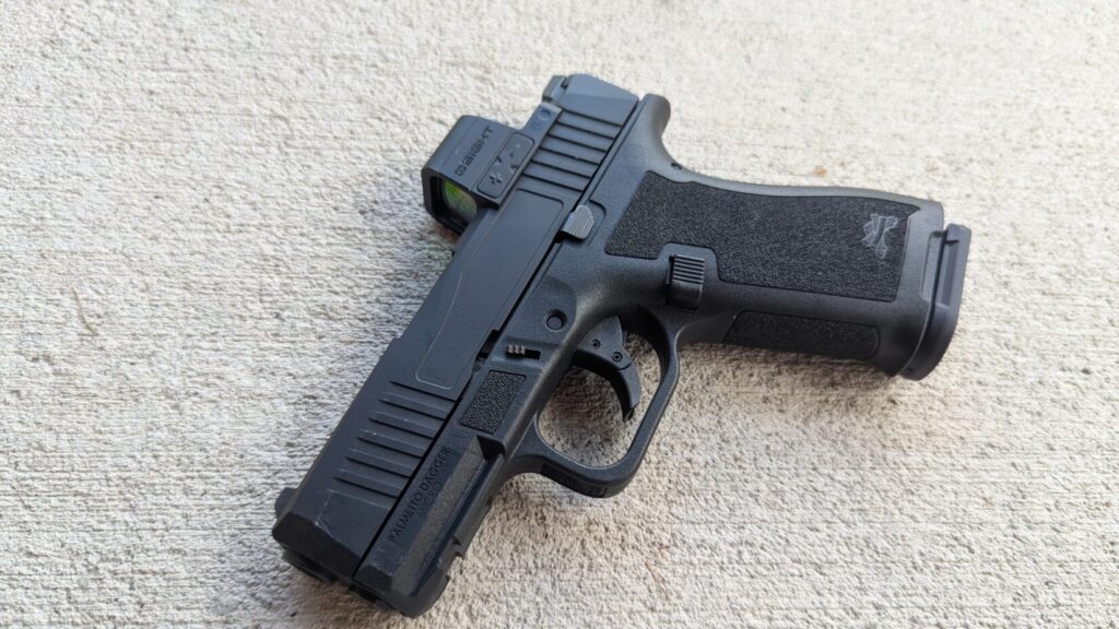 A PSA Micro Dagger pistol with an attached red dot optic resting on a concrete surface.