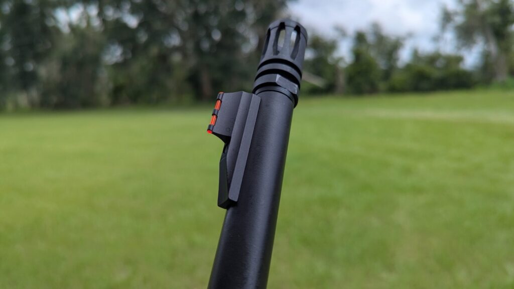 A close-up of the Mossberg MVP Patrol rifle's muzzle device and front sight, with a grassy field in the background.