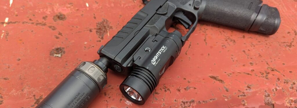 An Echelon pistol with a Nightstick TWM-30-T light and a suppressor, lying on a red, rusty surface.