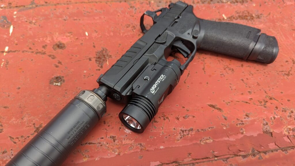 An Echelon pistol with a Nightstick TWM-30-T light and a suppressor, lying on a red, rusty surface.