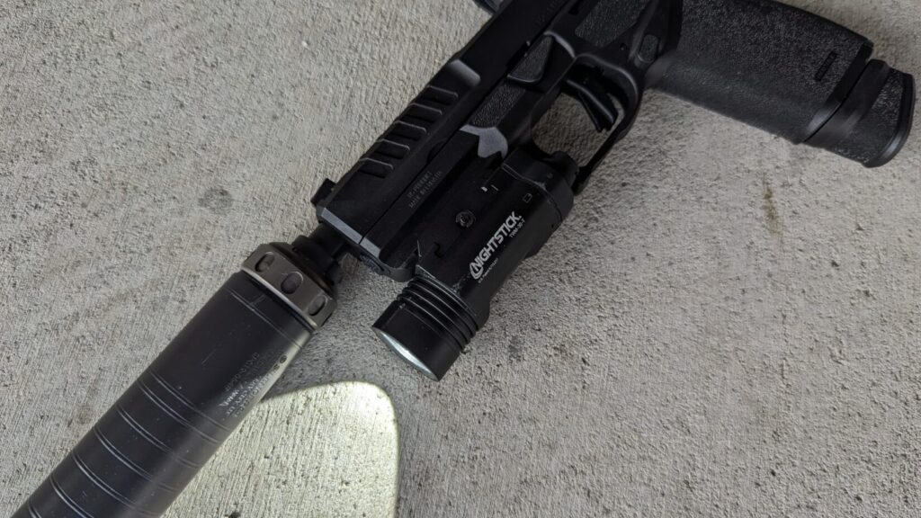 An Echelon pistol with a Nightstick TWM-30-T light and a suppressor, lying on a concrete surface.