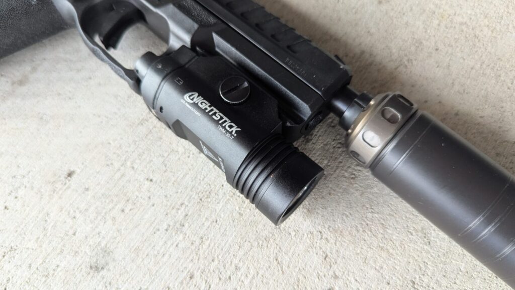 An Echelon pistol with a Nightstick TWM-30-T light and a suppressor, lying on a concrete surface.