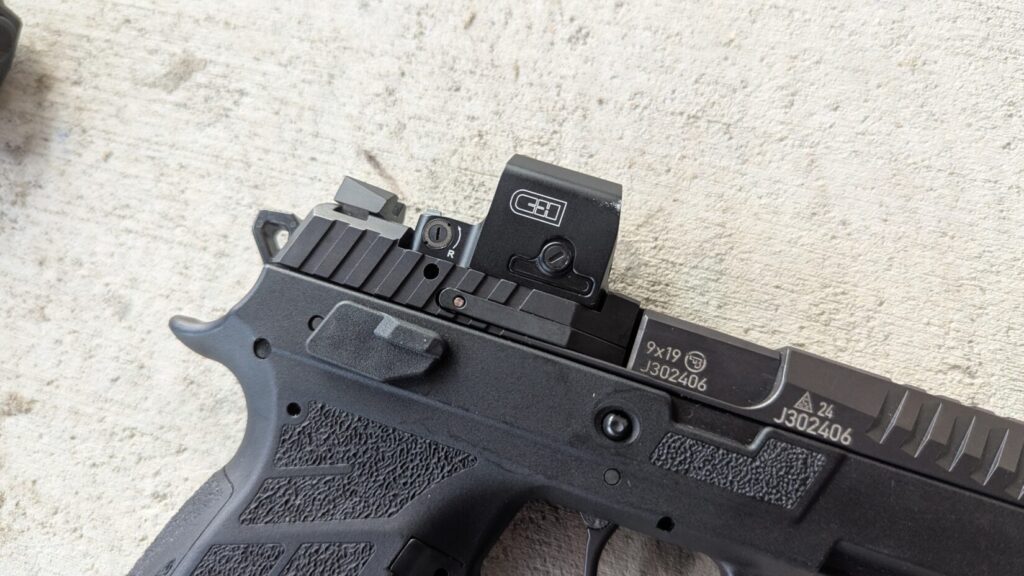 Close-up of a black handgun with an EDC Enclosed red dot sight mounted on the slide. The gun is a 9x19 model with serial numbers visible.