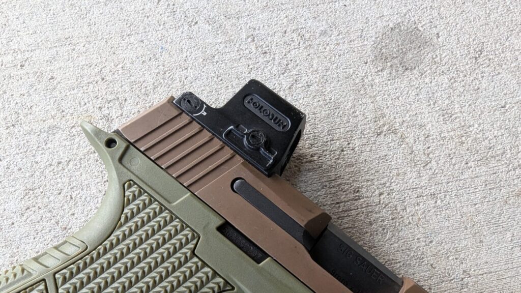 Close-up of a two-toned handgun (tan and green) with a Holosun EPS Carry red dot sight mounted on the slide.