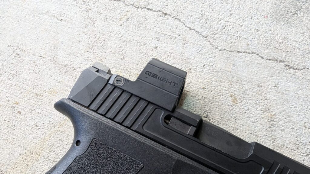 Close-up of a black handgun with an Osight S red dot sight on a textured surface.