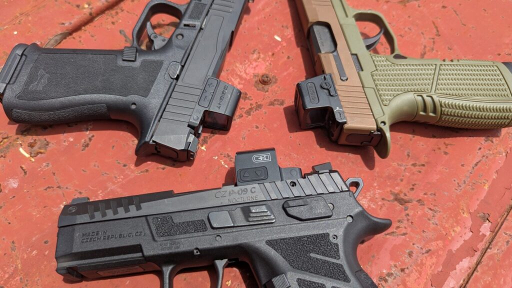 An angled shot of a PSA Micro Dagger pistol with a red dot optic, resting on a red textured surface.