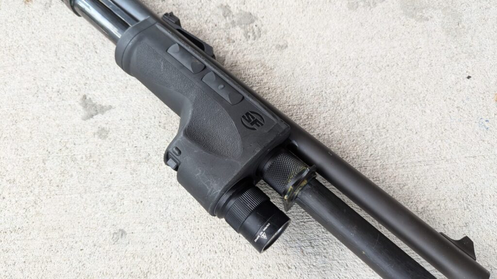 Close-up of the Surefire DSF weaponlight's forend and a single button on a shotgun, resting on a concrete surface.