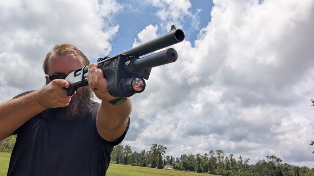 Person aiming a shotgun with a Surefire DSF weaponlight in a field. The shotgun's forend is visible, along with the person's hands.