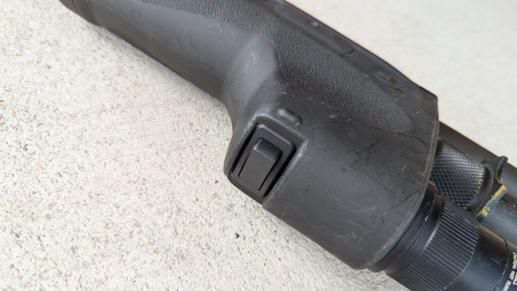 A close-up of a shotgun's forend with a Surefire DSF weaponlight and its kill switch on the bottom, resting on a concrete surface.
