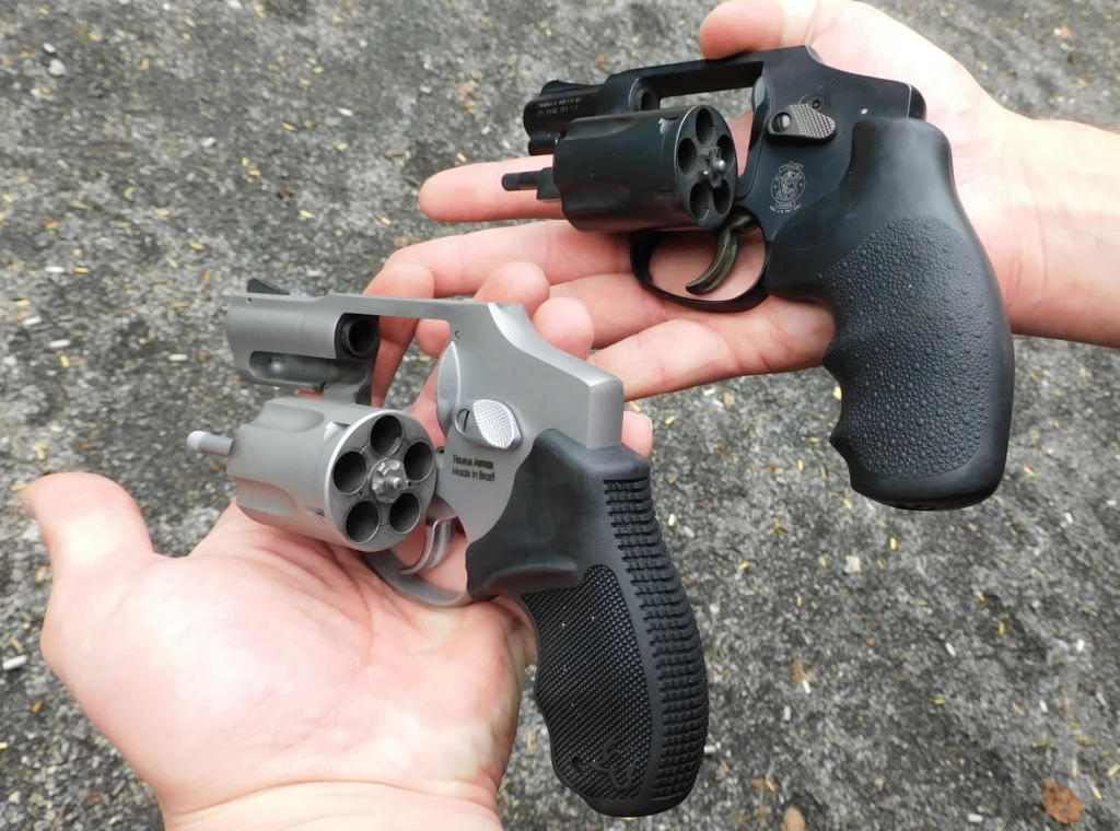 Taurus 850 and Smith and Wesson 442 revolvers held with open cylinders held by hands