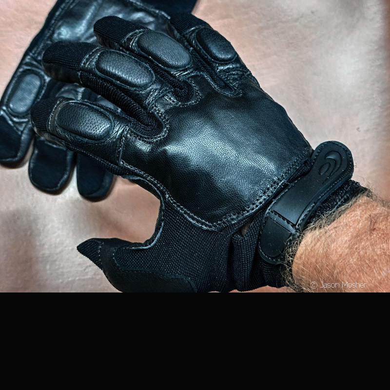 A close up view of a hand with a black glove on with padded areas over the fingers and knuckles. 