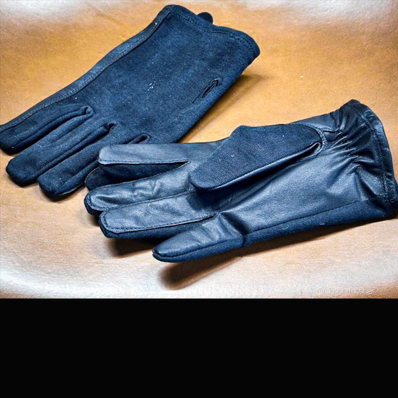 Two pair of black gloves laying on a light brown surface. 