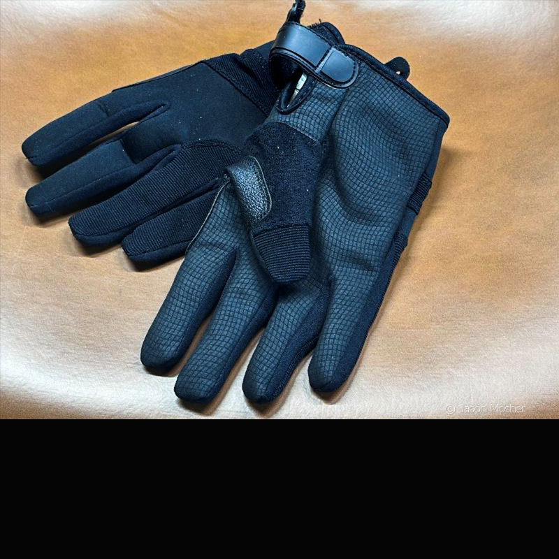 Two pair of black gloves laying on a brown surface. One glove is facing up and one facing down. 