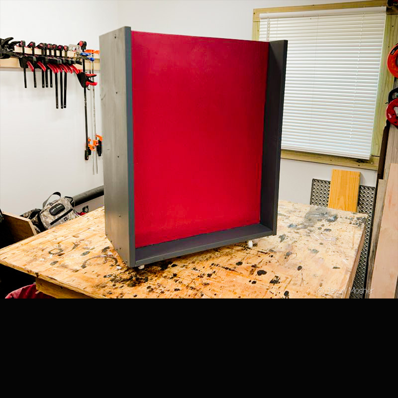 A holster caddy made of wood and painted grey with a red center panel. 