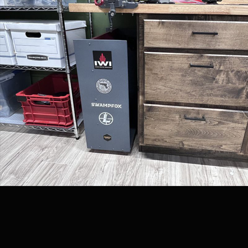 The edge of a grey holster caddy visible under a wood counter, beside a cabinet. 