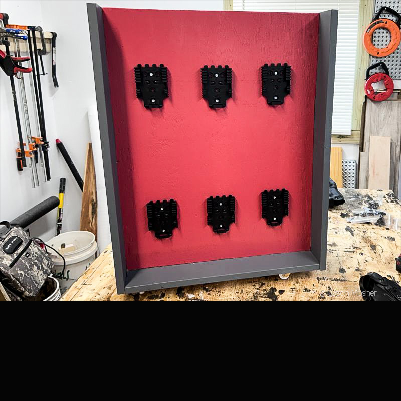 The holster caddy on a work bench with black plastic QLS plates screwed to the red backboard. 