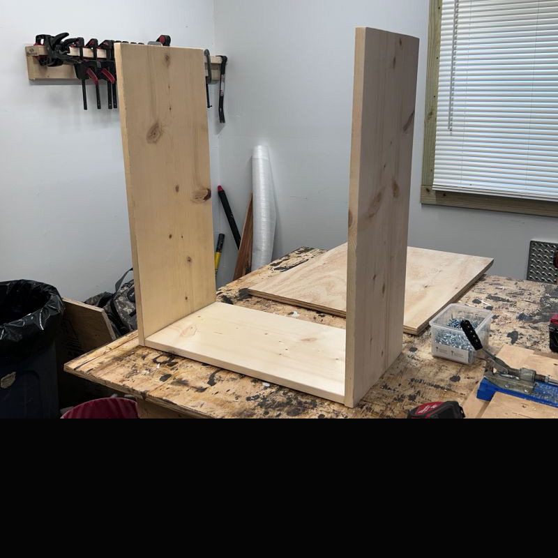 Two upright boards screwed to another board laying on a work bench. 
