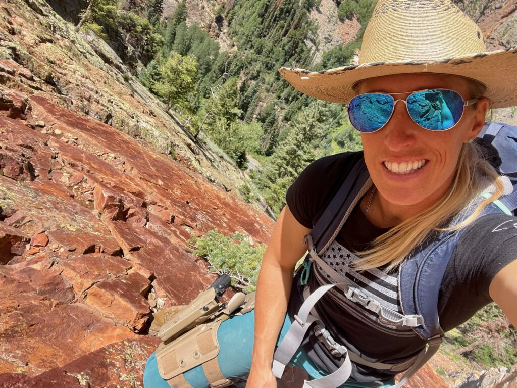 woman wearing straw hat, backpack, and double strap leg shroud with safariland holster attached via QLS