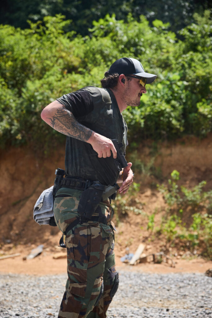 A man at a shooting range is shown in a profile view, drawing a handgun from a holster on his hip.