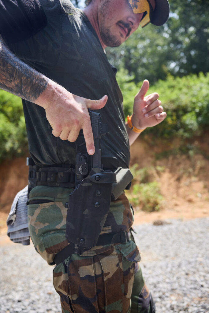 A close-up side view of a man drawing a handgun from a black camouflage Safariland holster worn on a tactical belt.