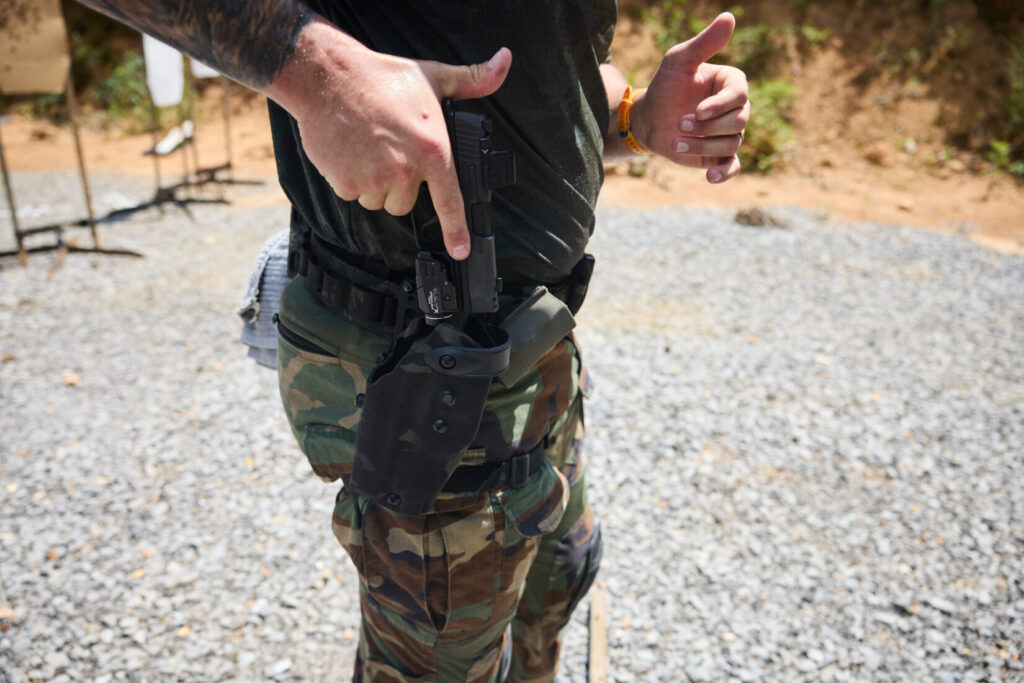 A close-up side view of a man drawing a handgun from a black camouflage Safariland holster worn on a tactical belt.