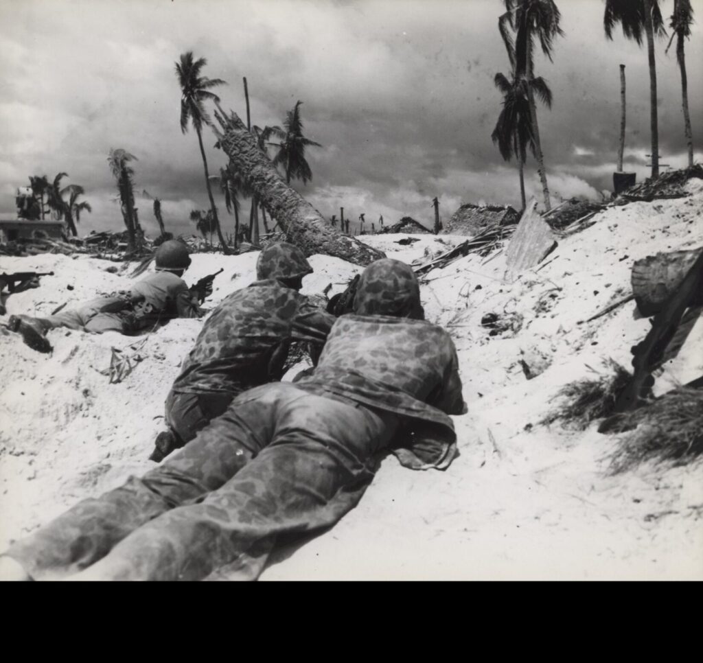 Marines landing on Tarawa Island beach creep up on Japanese pill boxes. The terrain of the island offered very little protective covering, but these Marines made use of what little covering there was. (Julian C. Smith Collection (COLL/202), Marine Corps Archives & Special Collections. CC BY-SA 2.0)