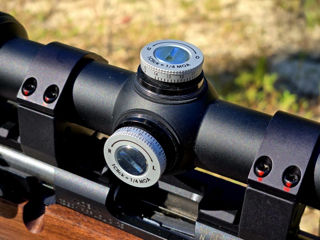 A rifle scope without caps showing 1/4 MOA adjustments.