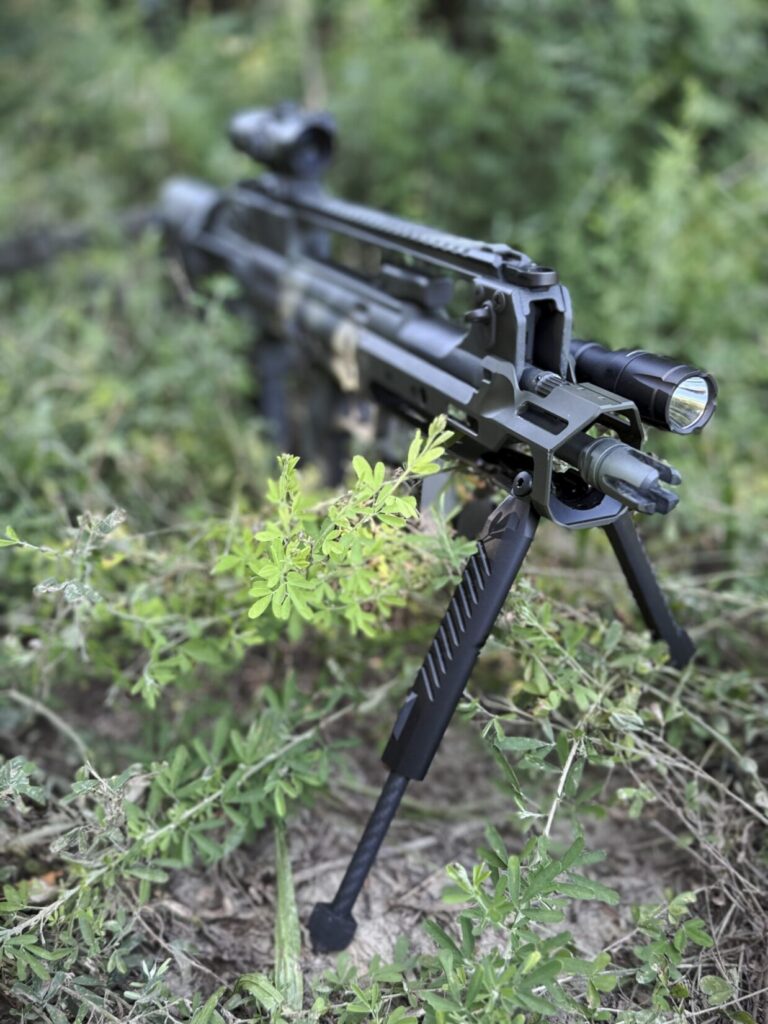 A front quartering-to photo of the Hellion in some brush with the Blk Lbl bipod deployed.