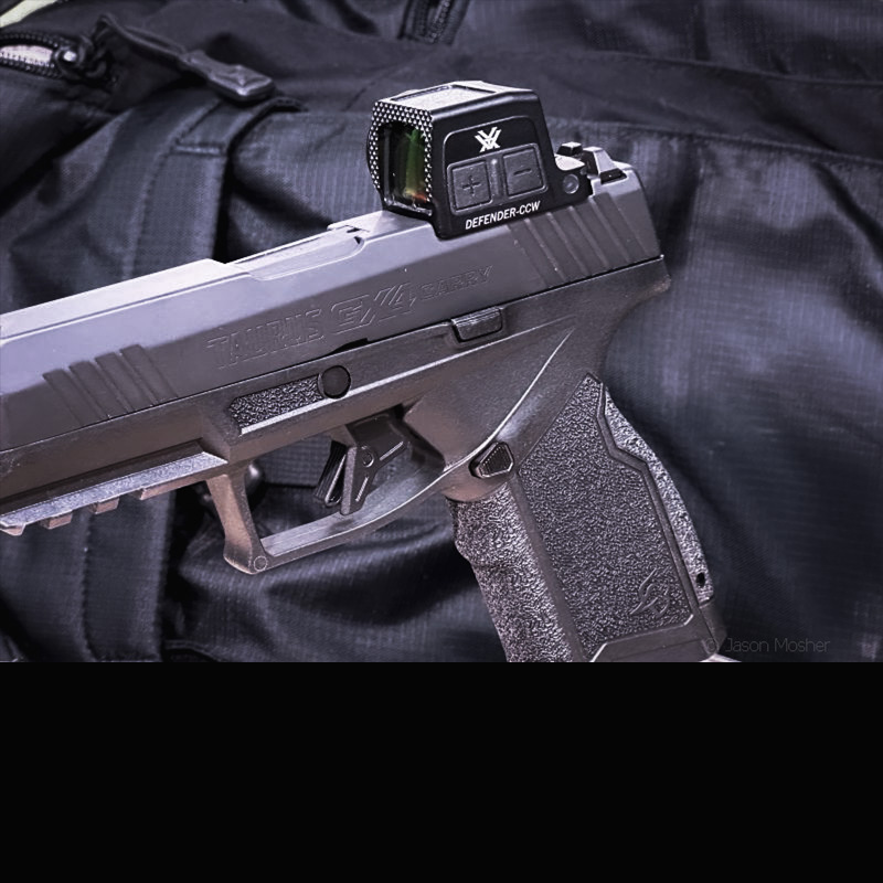 A Taurus GX4 Carry handgun with a Vortex Defender CCW mounted to it on a stand in front of a black background. 