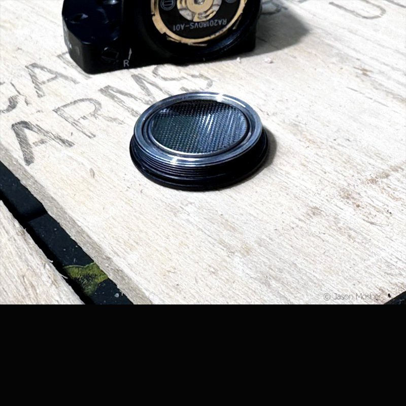 The battery cap of the Vortex Defender CCW laying on a wood box beside the optic. 