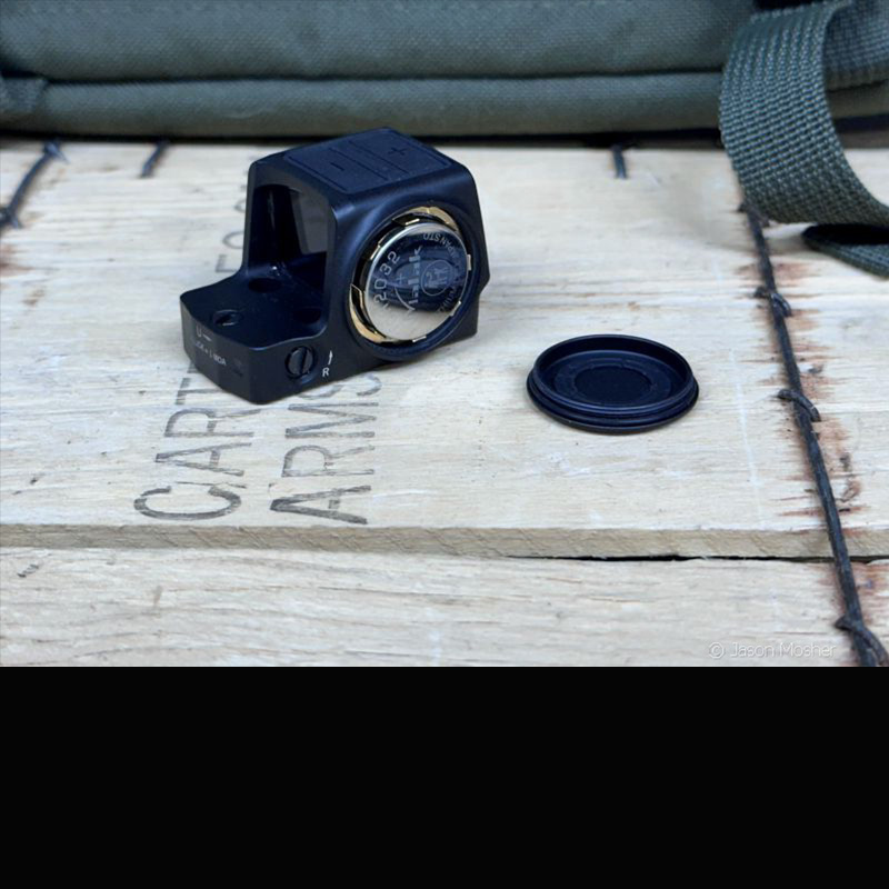 The Vortex Venom optic on a wood box with the battery lid off, lying beside it with the battery. 