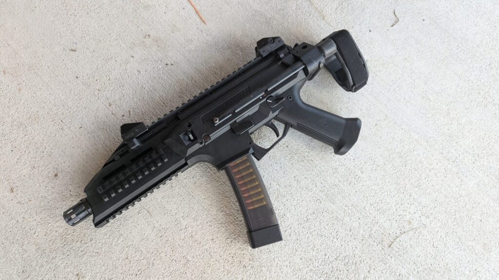 A black CZ Scorpion Evo 3 pistol with a brace and a loaded translucent magazine lies on a concrete surface.