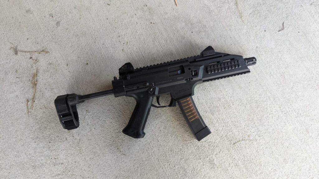 A black CZ Scorpion Evo 3 pistol with a brace and a loaded magazine rests on a concrete surface.