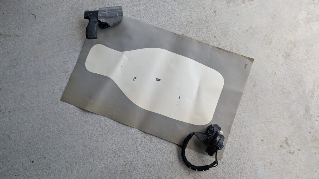 A gun, holster, ear protection, laid out on a paper shooting target.